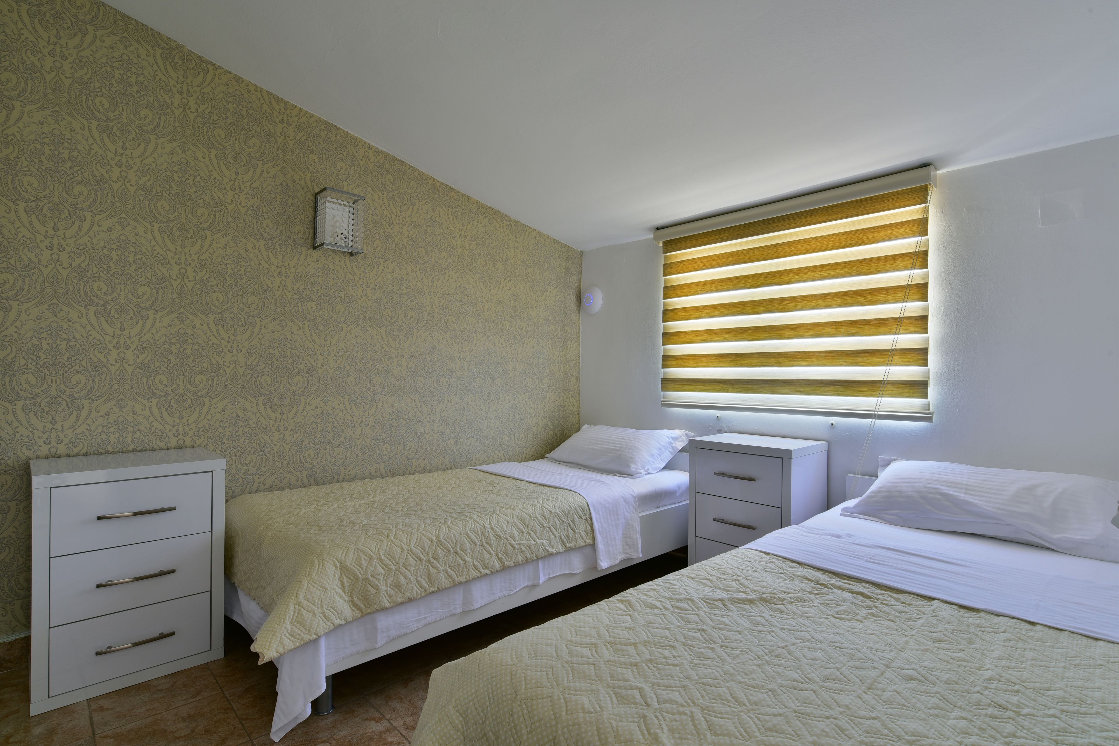 A bedroom with two beds, a nightstand, a dresser, and a window with blinds.