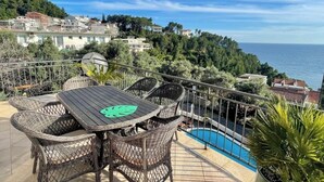 Una terraza con mobiliario de mimbre y piscina, con vistas a un pueblo costero.