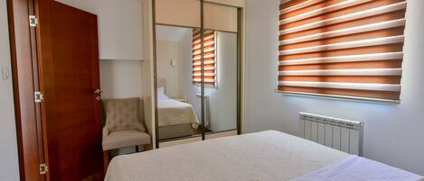 Un dormitorio con cama, una silla, un armario y una ventana con persianas.