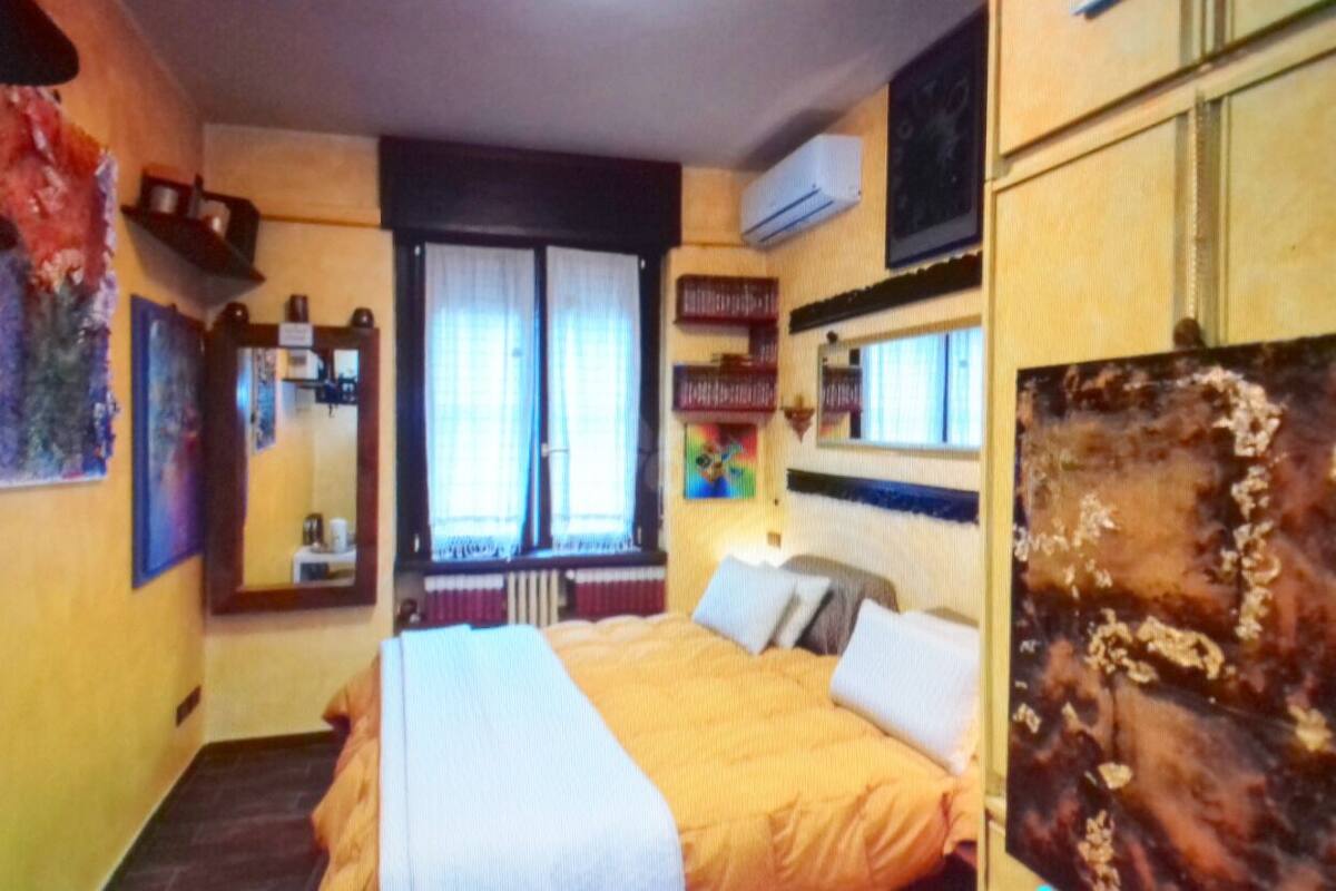 Ein Hotelzimmer mit Bett, einem Fenster mit Vorhängen, einem Bücherregal und einem an der Wand befestigten Fernseher.