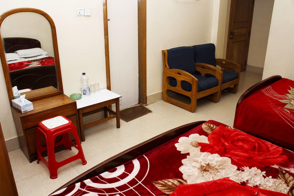 A bedroom with a bed, a wooden desk, a chair, a mirror, and a small stool.
