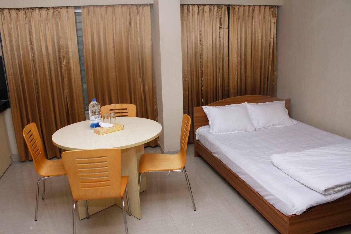 Una habitación de hotel con una cama, una mesa redonda con sillas y cortinas.