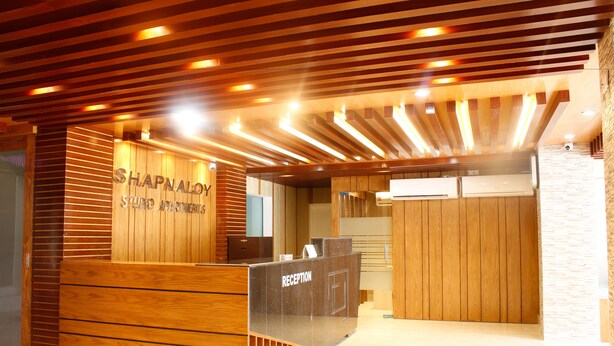 Un espace d’accueil avec un comptoir de réception en bois portant l’inscription « Shapnaly Studio Apartments ».