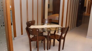 Un coin repas avec une table en verre et quatre chaises en bois, une cloison en bois avec des lattes verticales, et un lit à l’arrière-plan.