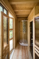 Un interior de madera con ducha cubierta por vidrio, ventanas amplias y suelo de madera.