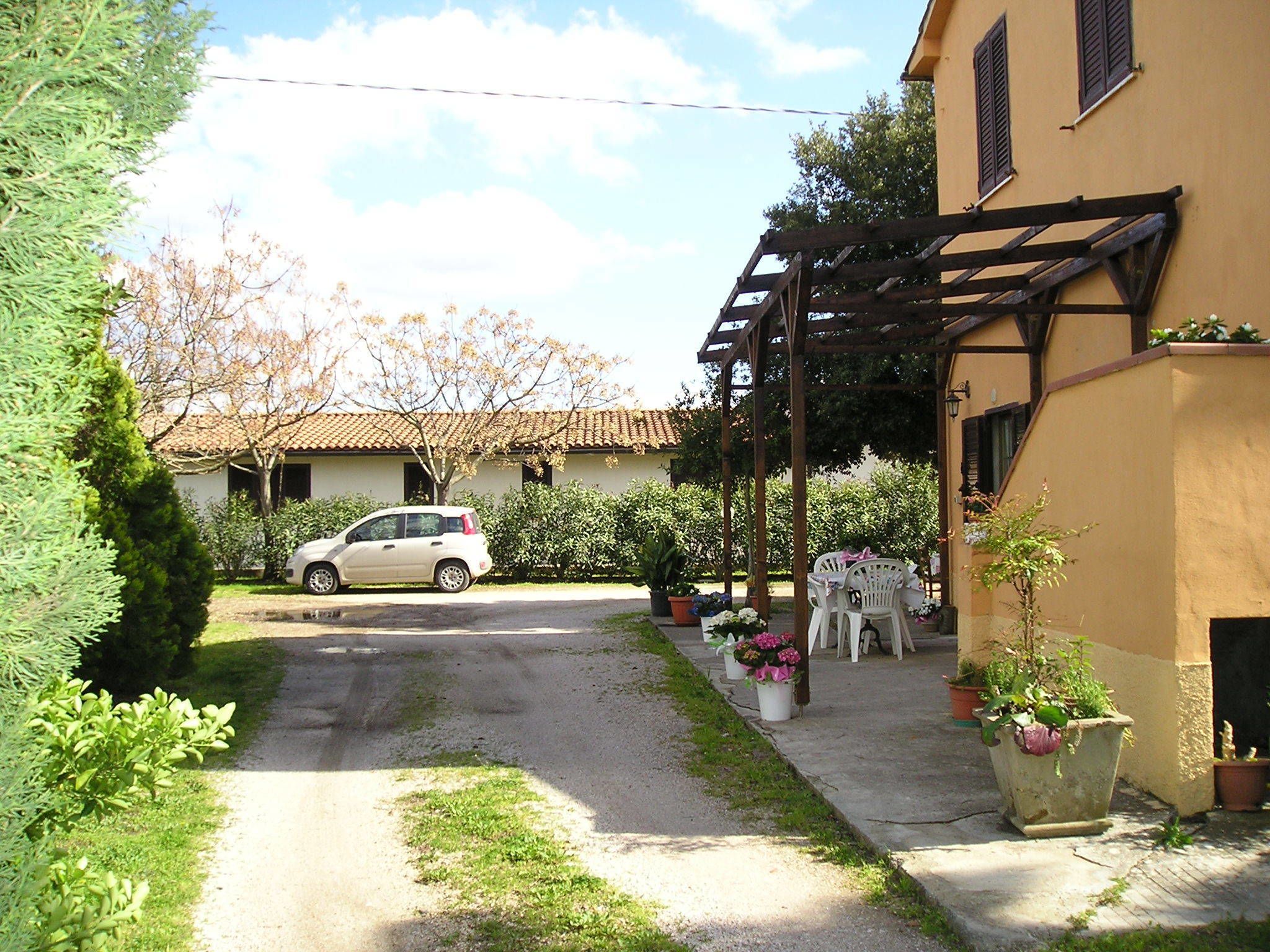 Ein Wohngebiet mit einem geparkten Auto vor einem Haus, einem Garten mit Blumentöpfen und einer Pergola.