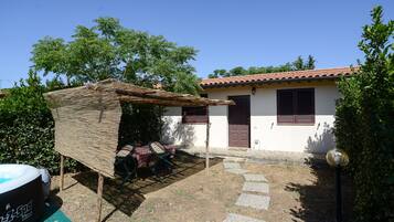A small house with a tiled roof, a covered patio with a table and chairs, and a swimming pool.