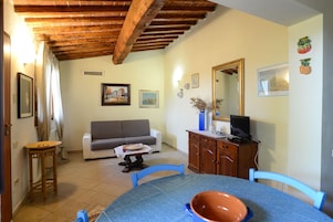 Una sala de estar con techo de madera, un sofá, una mesa de comedor con sillas, un televisor y un aparador.