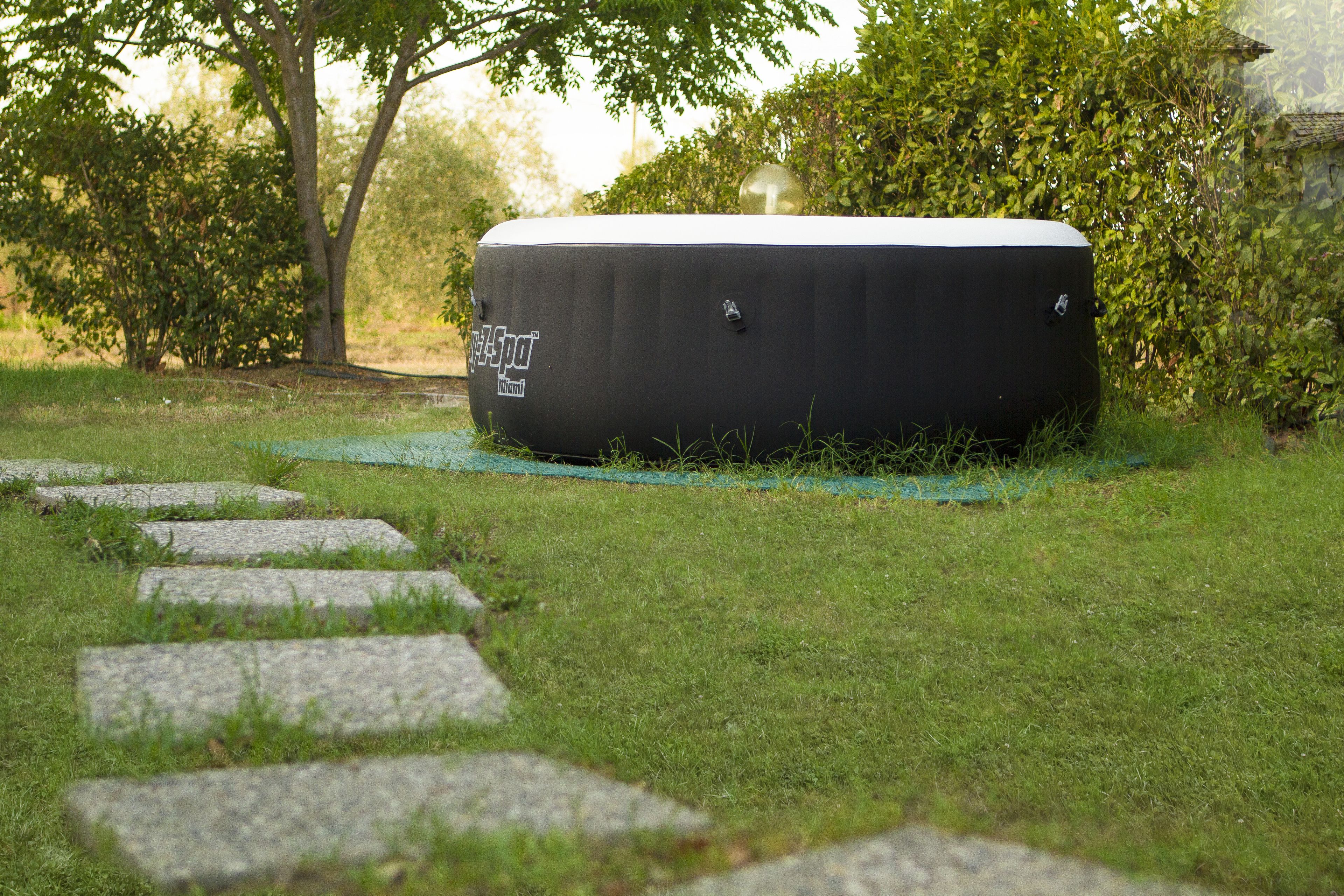 A spa pod labeled "SpaSpa Miami" on a grassy area with stone steps leading up to it, surrounded by greenery.