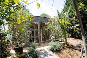 Una estructura de cristal con un muelle de madera, rodeada de diversas plantas y un jardín.