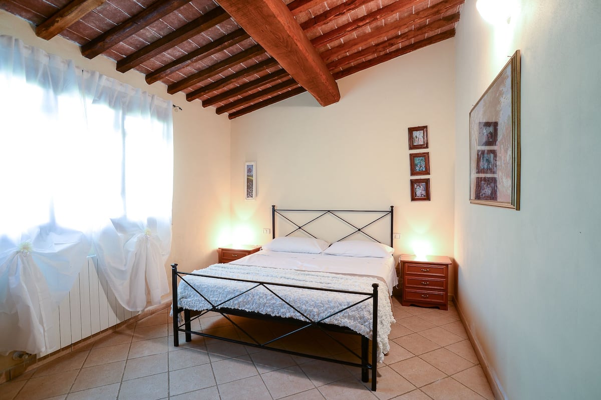 Quarto com cama, mesas de cabeceira e teto com vigas aparentes.