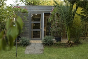 Una casa pequeña y moderna con puerta corredera de vidrio, rodeada de abundante vegetación y un jardín cuidado.