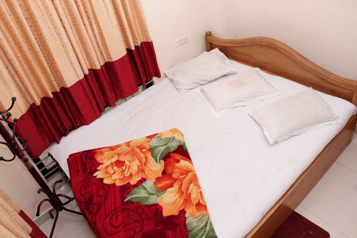 A neatly made bed with white linens and two pillows, a wooden headboard, and a floral-patterned blanket.