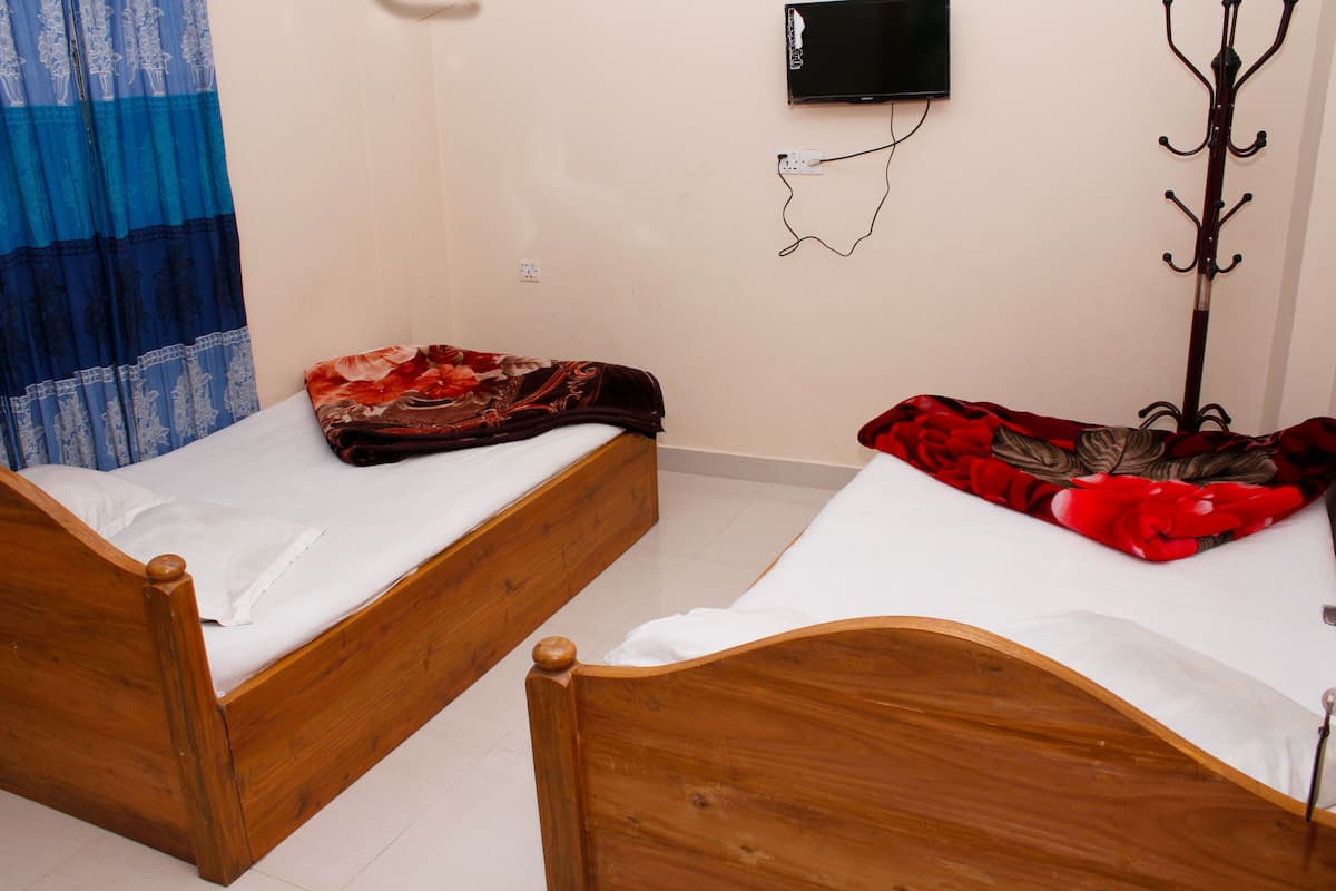 Two wooden beds with white linens, a blue and white curtain, a coat rack, and a wall-mounted TV.