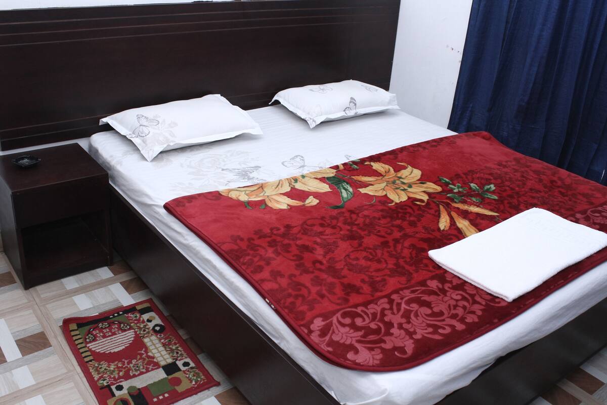 A neatly made bed with a floral bedspread and white pillows, a dark wooden headboard, and a small bedside table with a remote control.