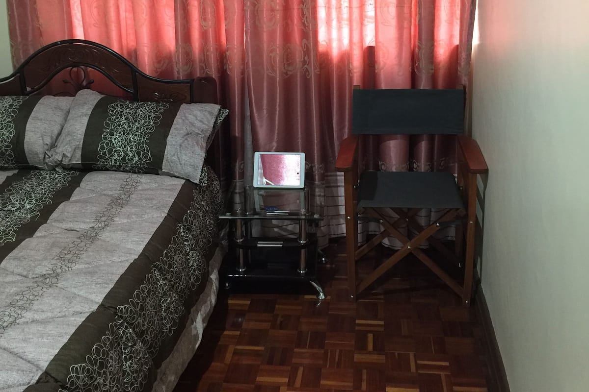A bedroom with a bed, a chair, a small table, and a curtain.