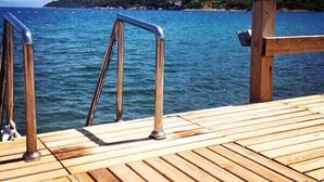 A wooden dock with metal railings leading into a calm body of water, surrounded by a hilly landscape. - Gunisigi Otel (Bodrum)