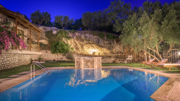 Una piscina con un muro de piedra, una terraza de madera y una estructura de piedra en el centro.