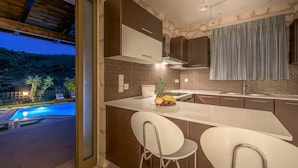 Una cocina moderna con una isla grande, taburetes de bar y vista a una piscina al anochecer.