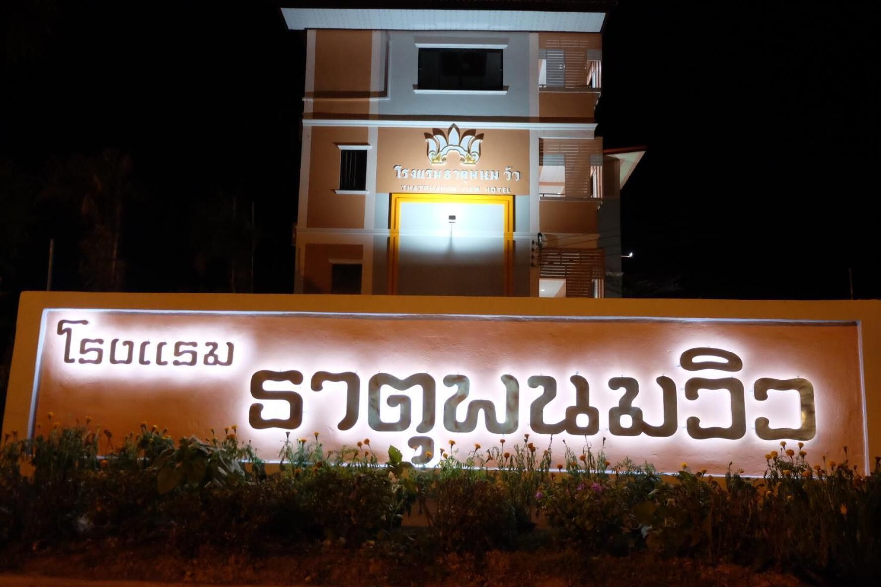 A hotel sign with Thai script and a modern building in the background.