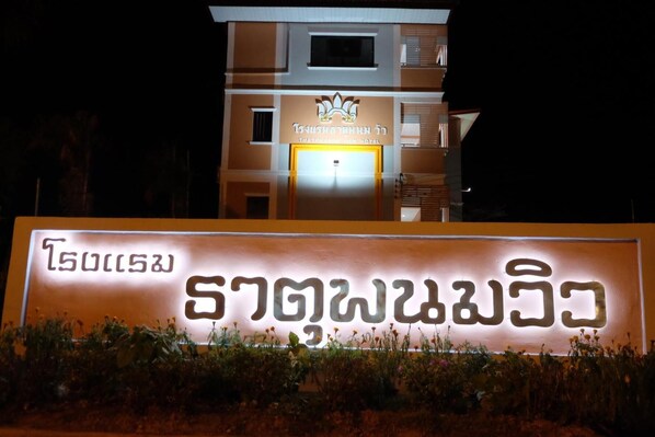 A hotel sign with Thai script and a modern building in the background.