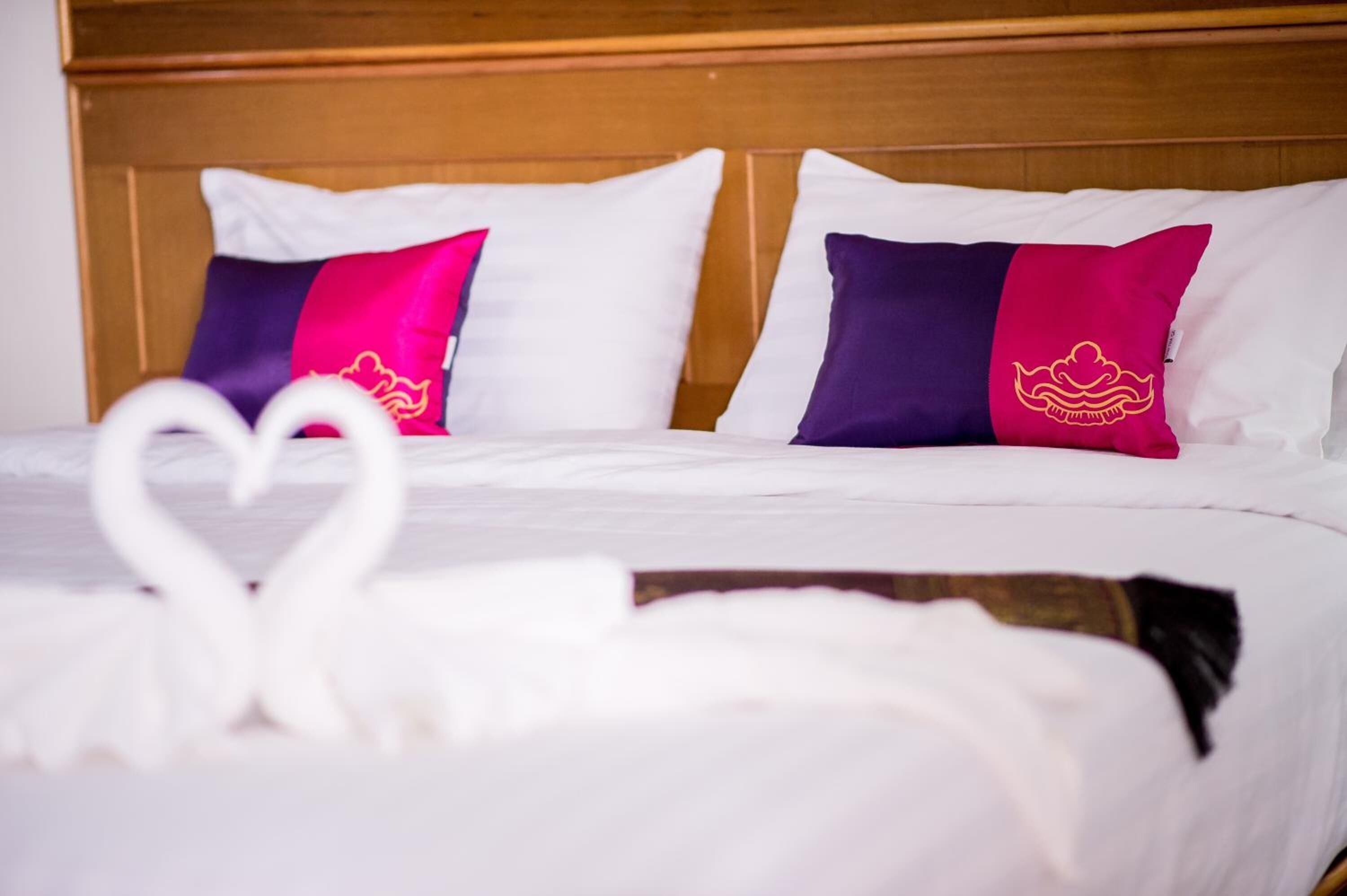 A neatly made bed with white bedding and two pillows, one with a pink and purple design and the other with a pink and dark purple design.