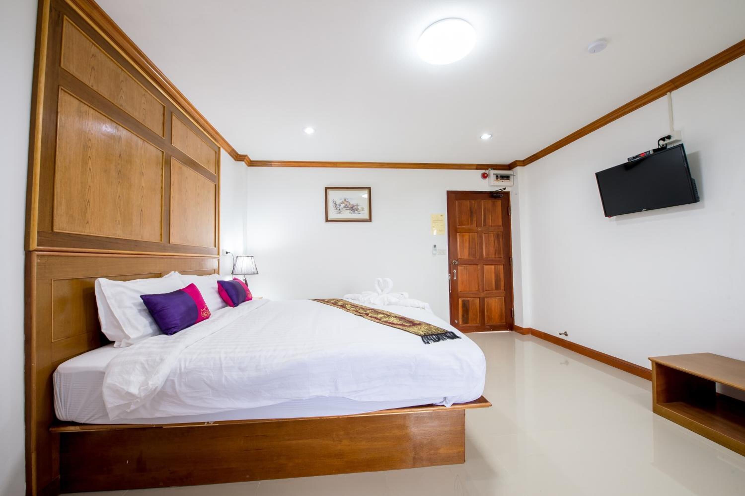 Un dormitorio con cabecera de madera, cama con ropa blanca, televisor montado en la pared y una puerta de madera.