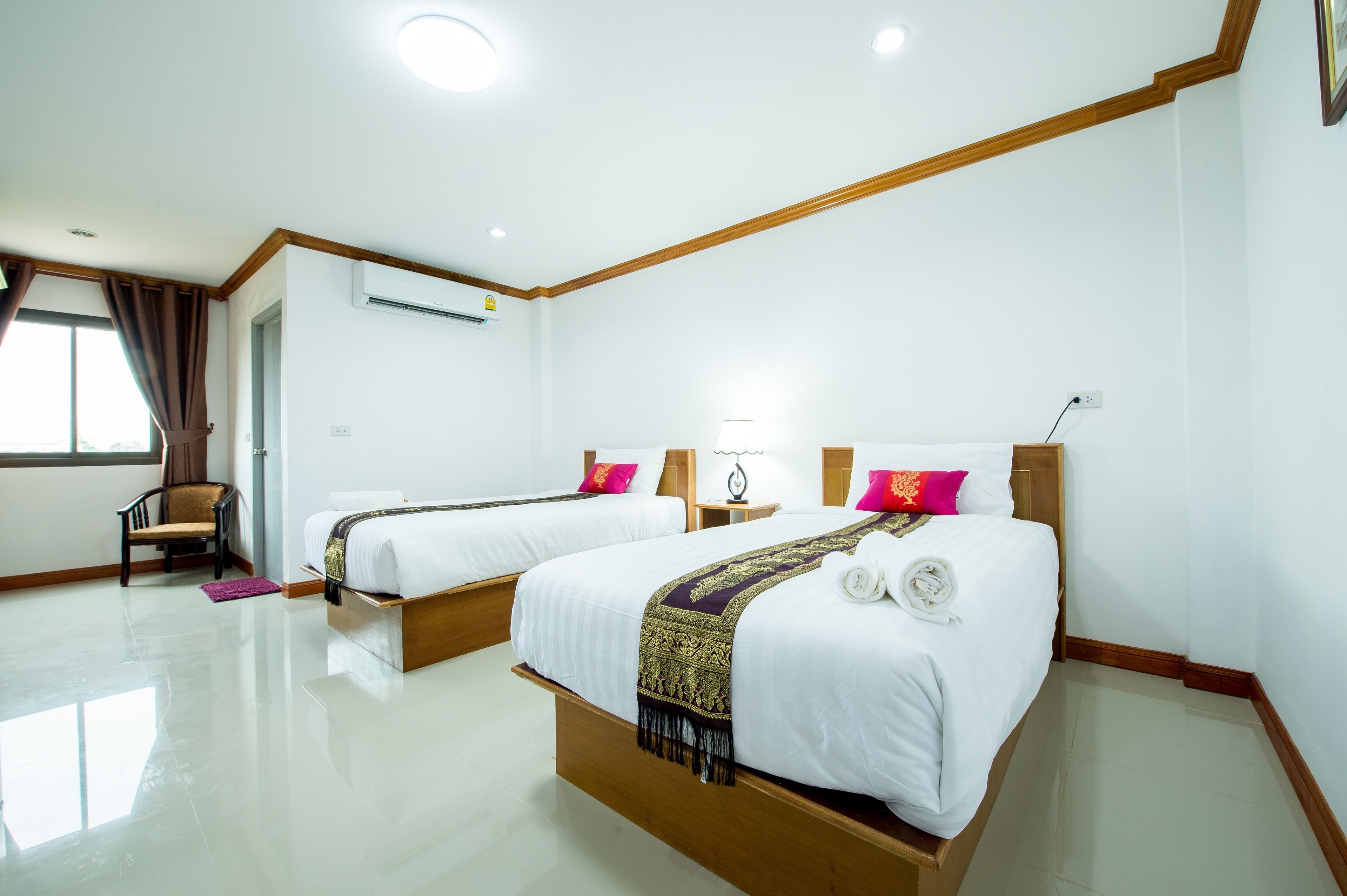 Habitación de hotel con dos camas, una silla, una lámpara y un ventanal con cortinas.
