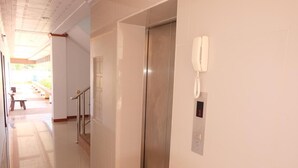Een nette, moderne hal met een glanzende lift en een telefoon aan de muur.