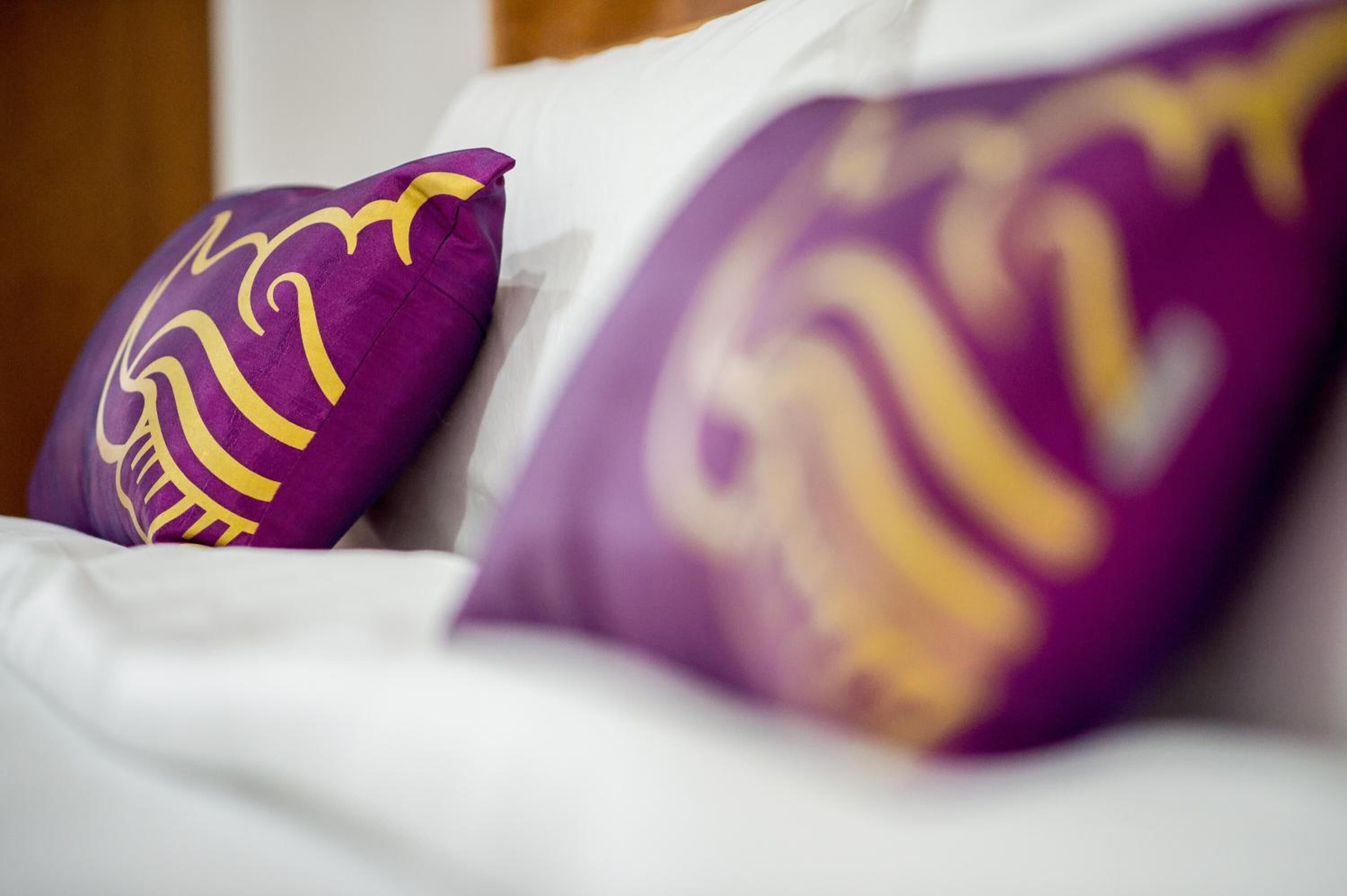 A bed with white bedding and purple pillows with yellow designs.