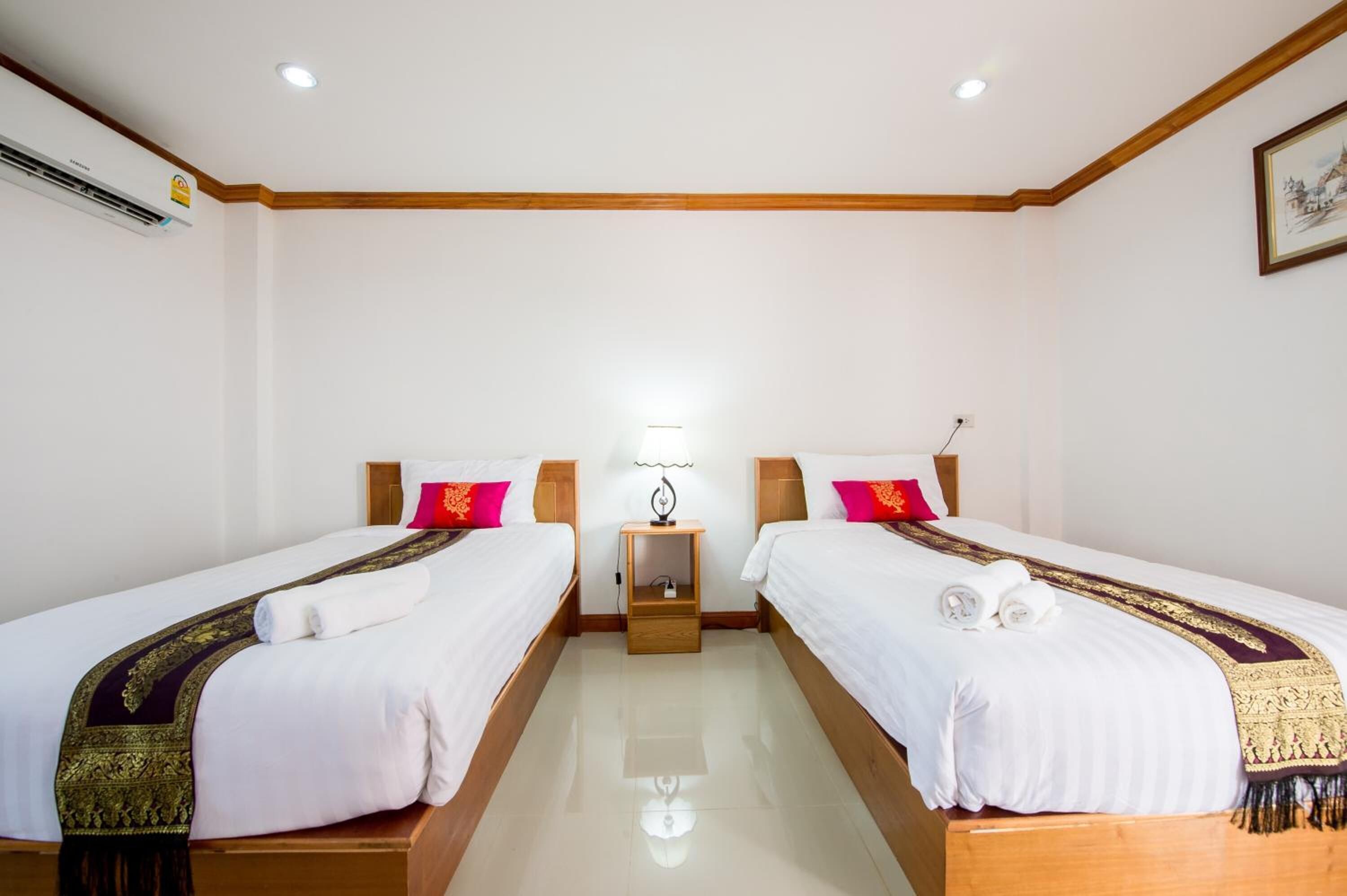 A hotel room with two beds, a nightstand with a lamp, and a wall-mounted air conditioner.