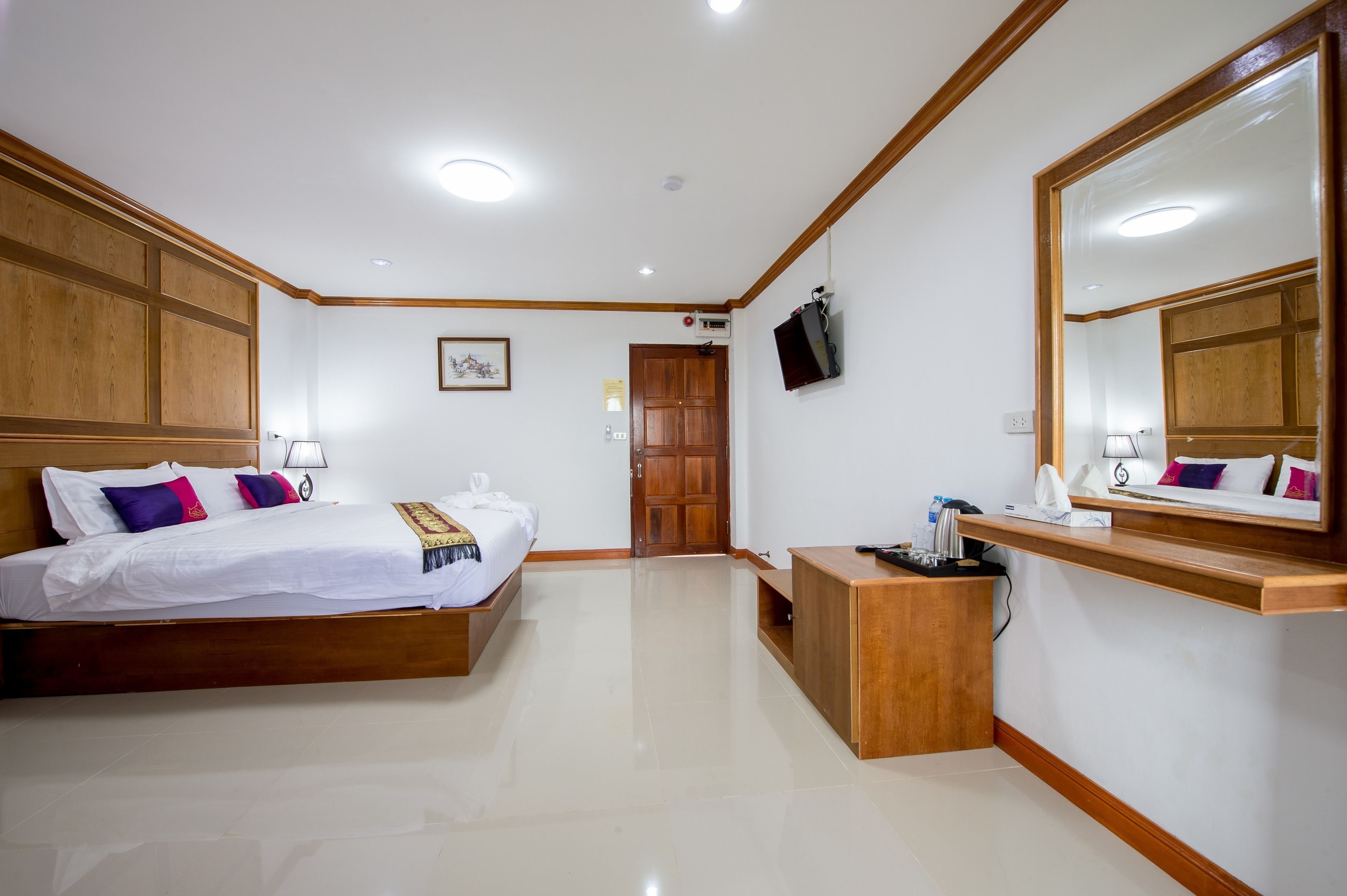 Une chambre d’hôtel avec un lit en bois, un bureau, un miroir et un téléviseur fixé au mur.