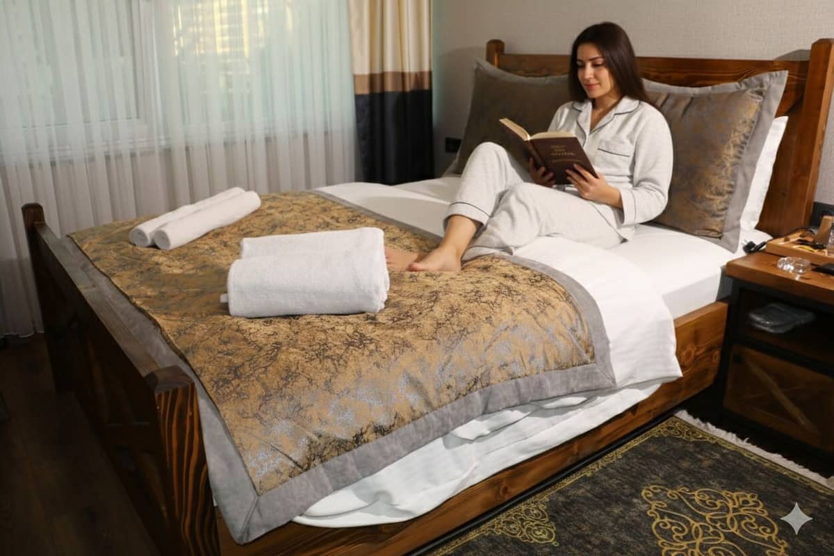 A bed with a patterned bedspread, a rolled towel, and a book.