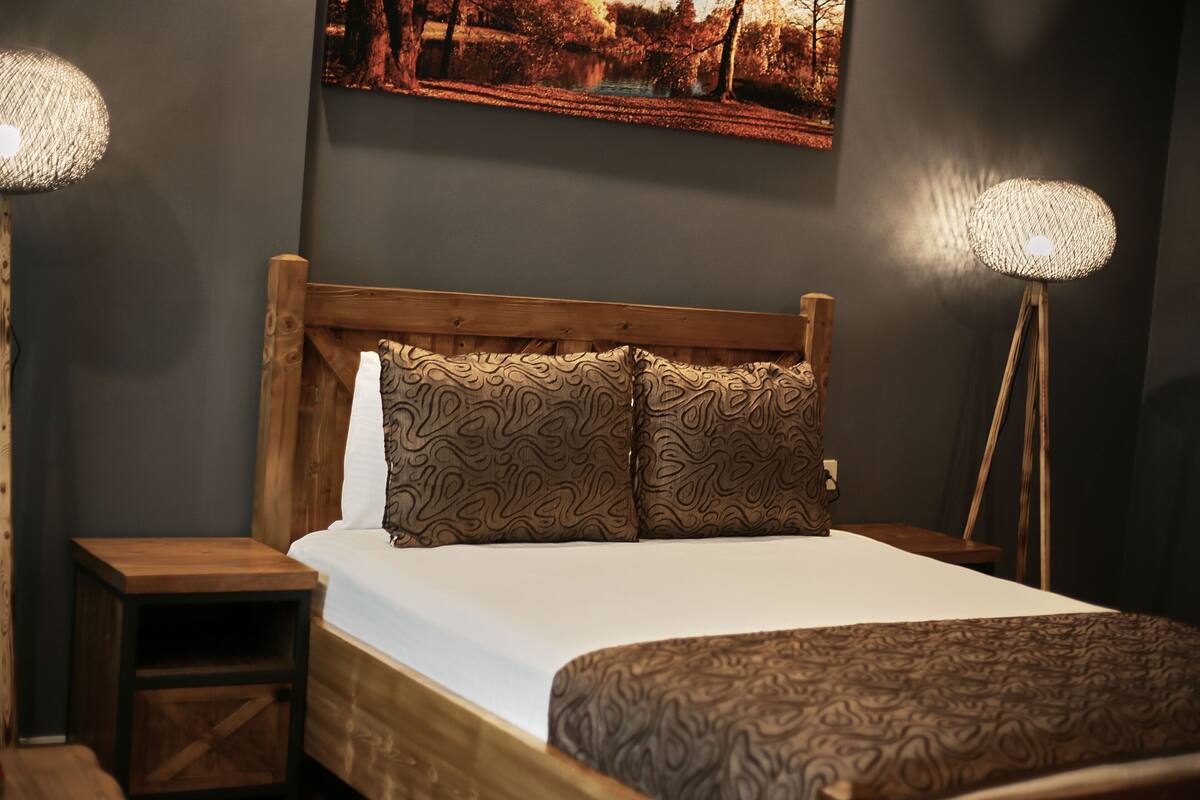 A bedroom with a wooden bed, patterned pillows, a nightstand, and a floor lamp.