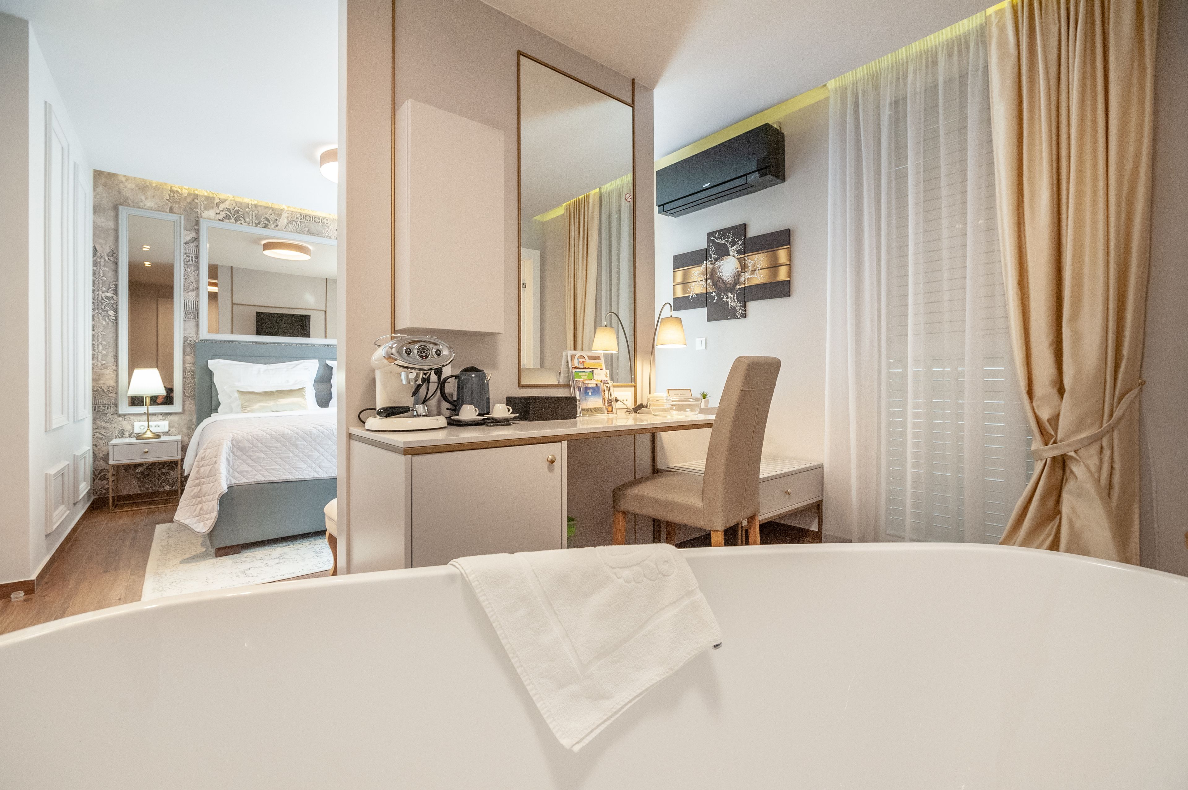 Ett hotellrum med en säng, ett skrivbord, en stol, en spegel och ett fönster med gardiner.