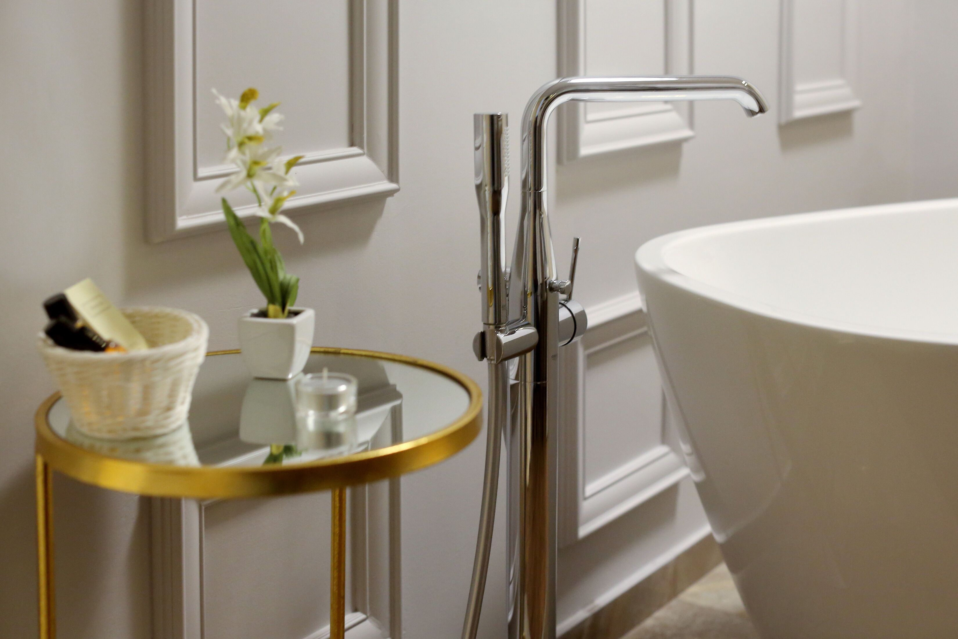 Un baño con una bañera blanca, un espejo redondo con marco dorado y una orquídea blanca en maceta.