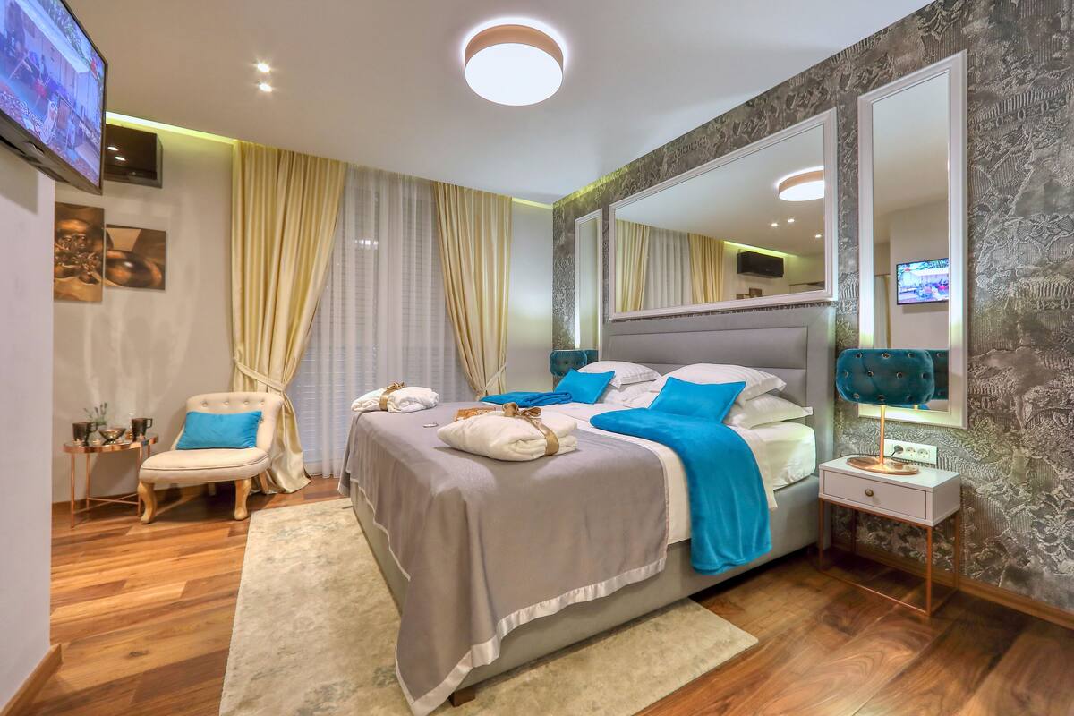 A modern bedroom with a large bed, a side table, a chair, and a TV.