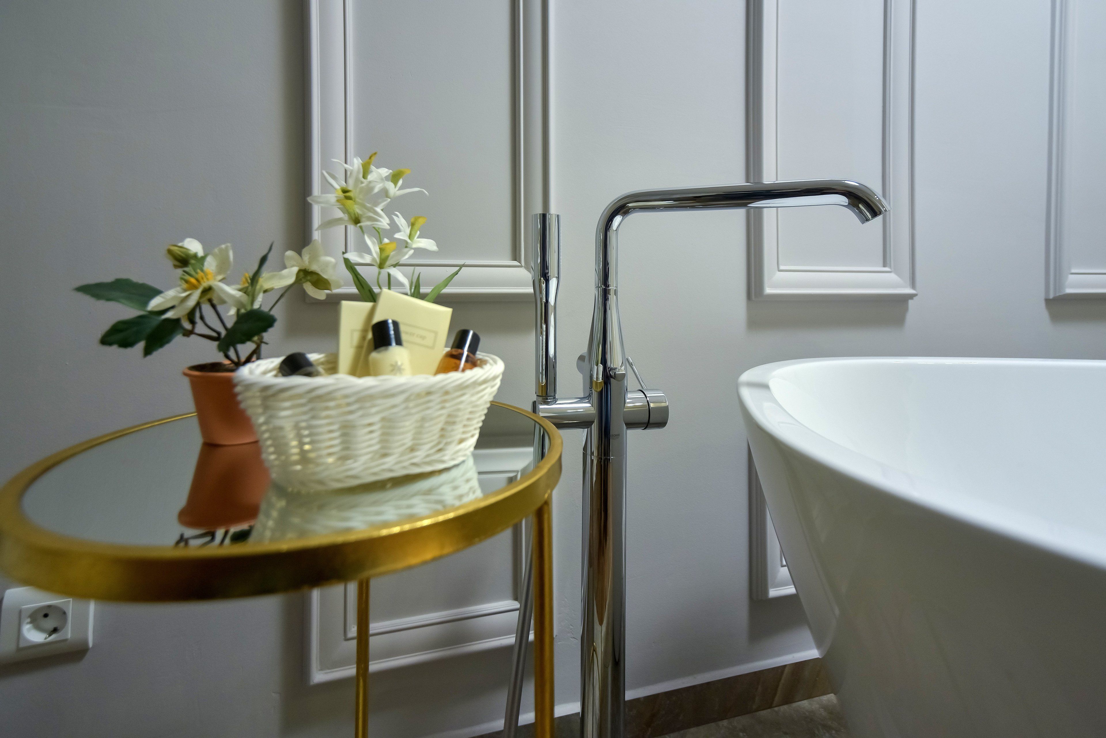 Une salle de bain avec une baignoire blanche, un miroir encadré d’or et une petite table sur laquelle sont posés une plante et des articles de toilette.