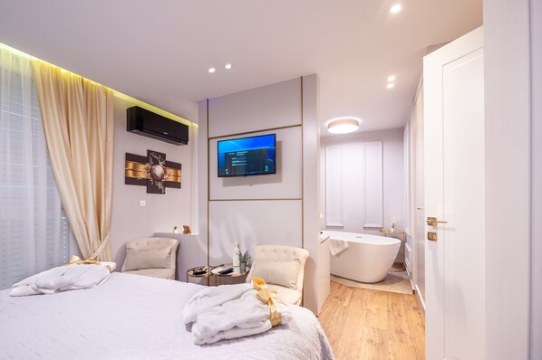 A modern hotel room with a large bed, a flat-screen TV, a bathtub, and a small side table with a remote control. - Luxury Rooms Kadena (Zadar)
