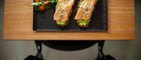 Two open-faced sandwiches on a black slate plate, garnished with sprouts and cherry tomatoes, placed on a wooden table.