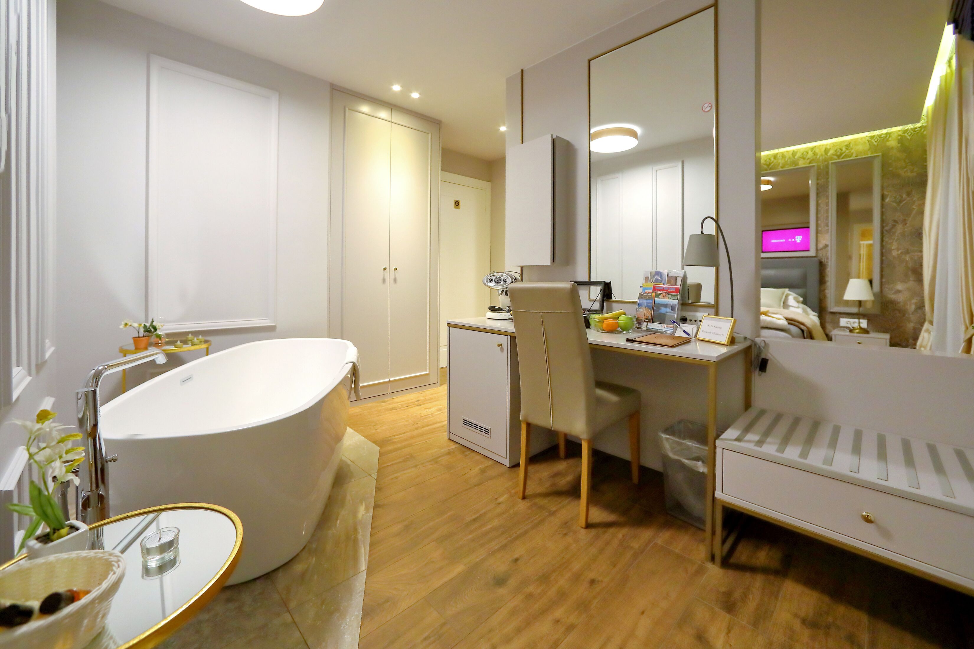 A modern bathroom with a freestanding bathtub, a desk with a chair, and a small cabinet.
