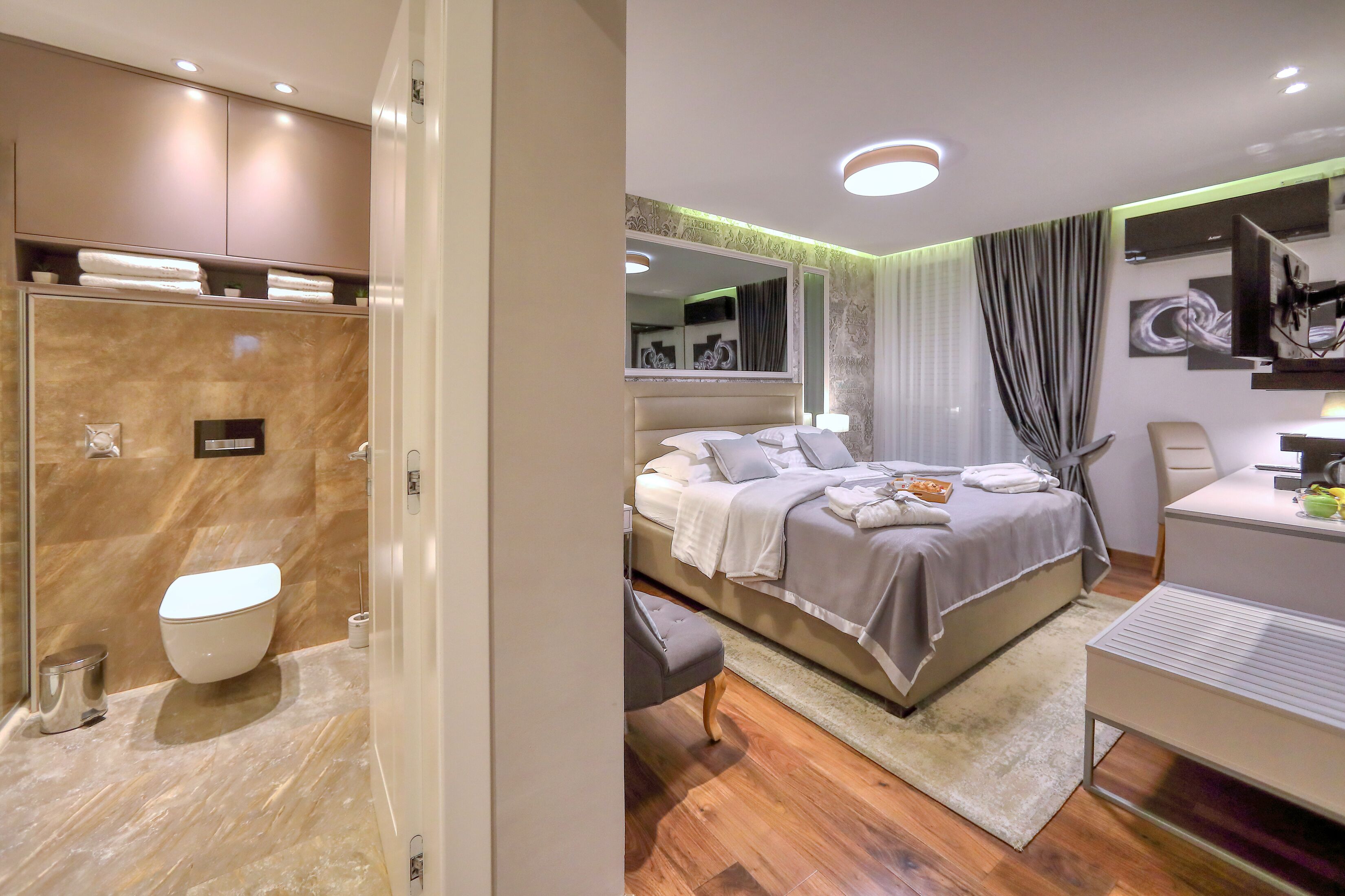 Een moderne hotelkamer met een marmeren badkamer, een bed met een grote spiegel en een bureau met een stoel.