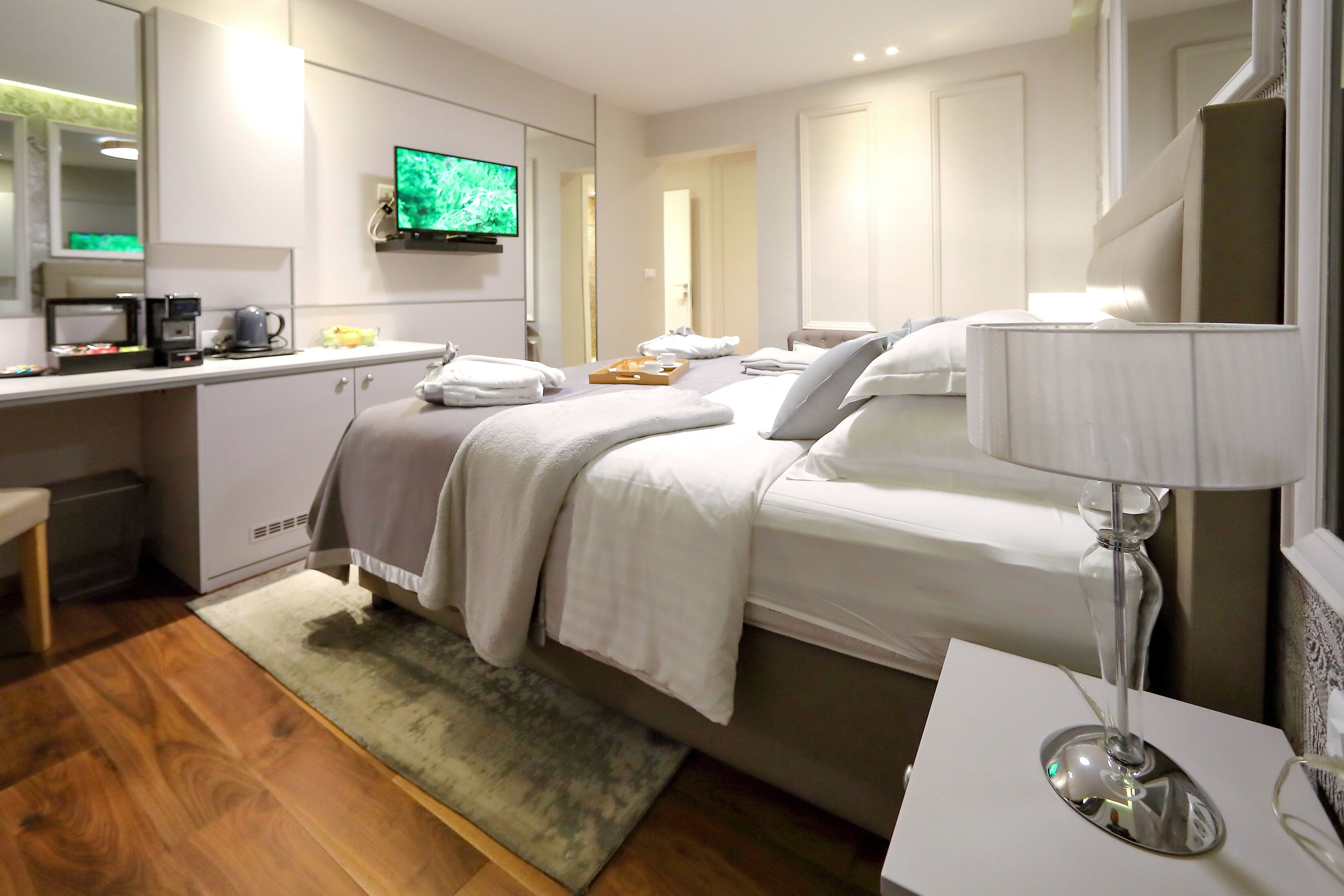 A modern hotel room with a bed, bedside table, lamp, and a TV on a stand.