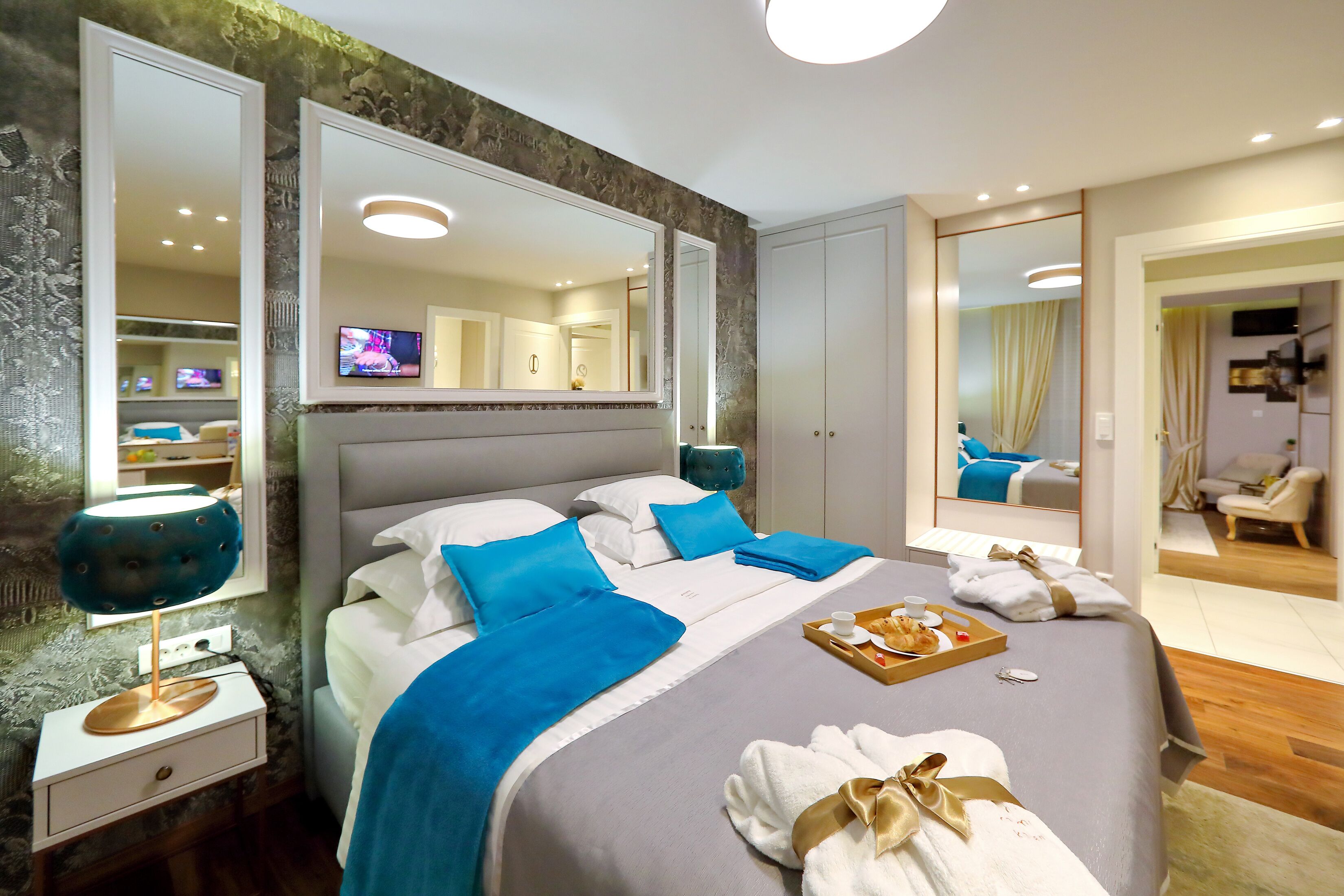 A modern hotel room with a large bed, a bedside table with a lamp, a mirror, and a TV.