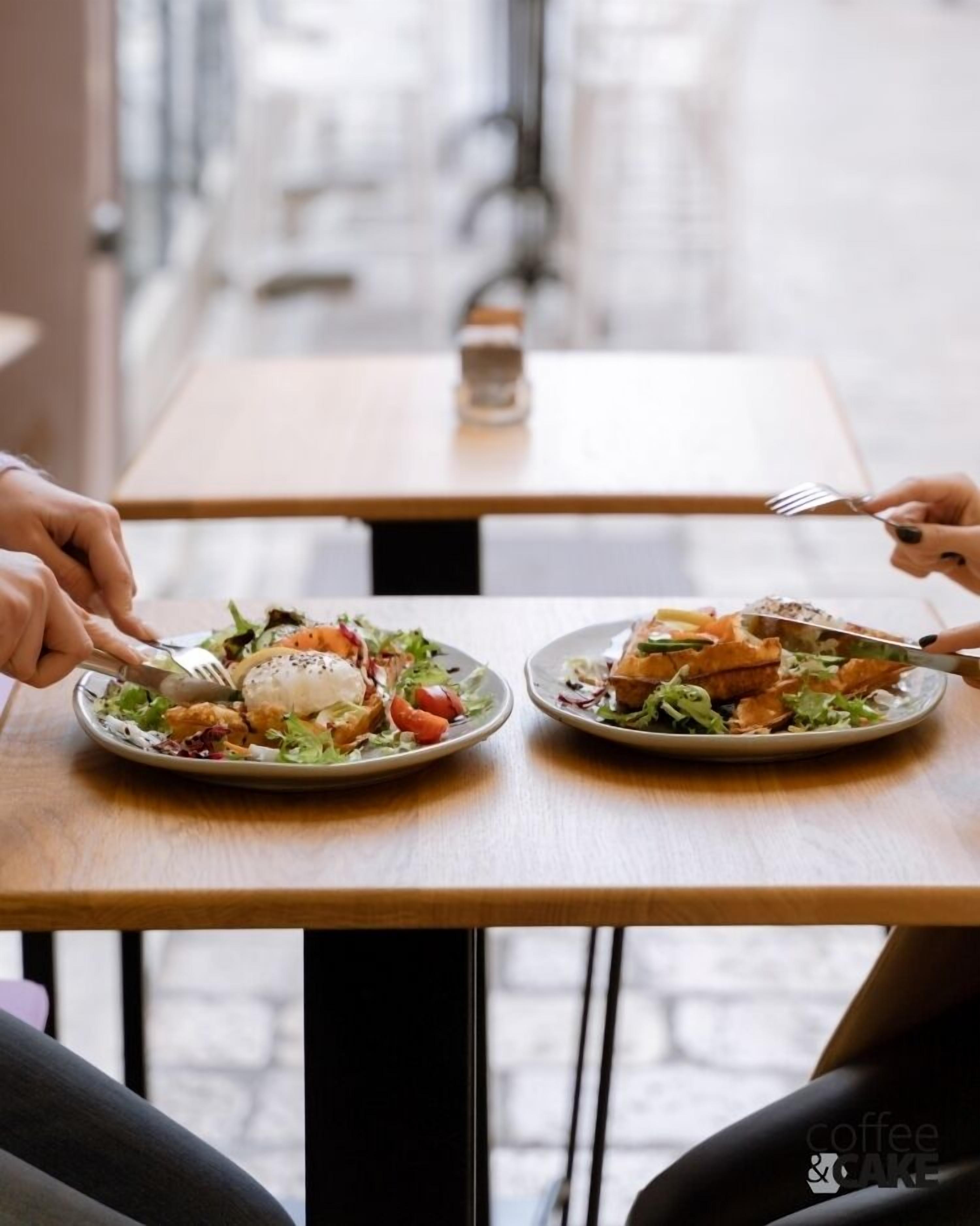 A restaurant setting with two plates of food on a table, a salt shaker, and a glass of water.