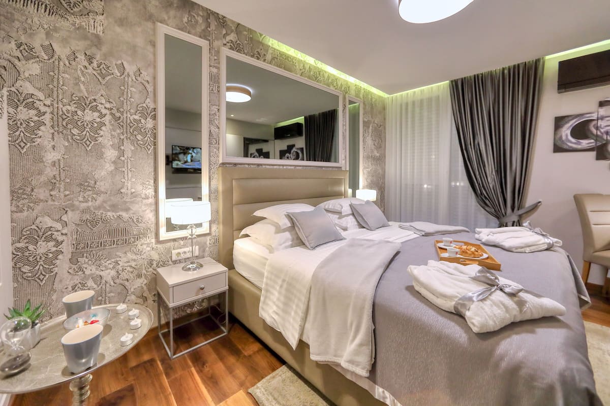 A modern hotel room with a large bed, a bedside table with a lamp, a mirror, and a decorative wall.