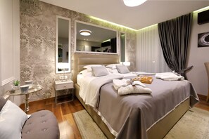 A modern hotel room with a large bed, a bedside table, a small round table with a plant, and a large mirror above the bed. - Luxury Rooms Kadena (Zadar)