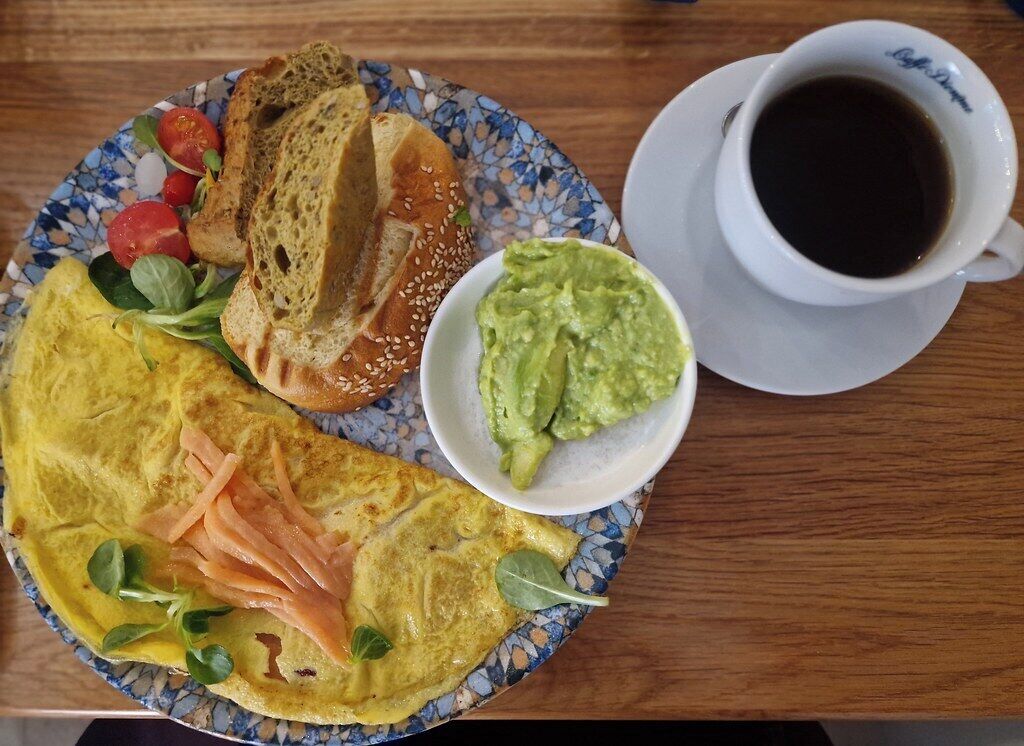 A plate with an omelette, bread, and avocado, and a cup of coffee on a table.
