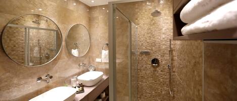 Un baño moderno con ducha envuelta en vidrio, dos lavamanos y un espejo grande.