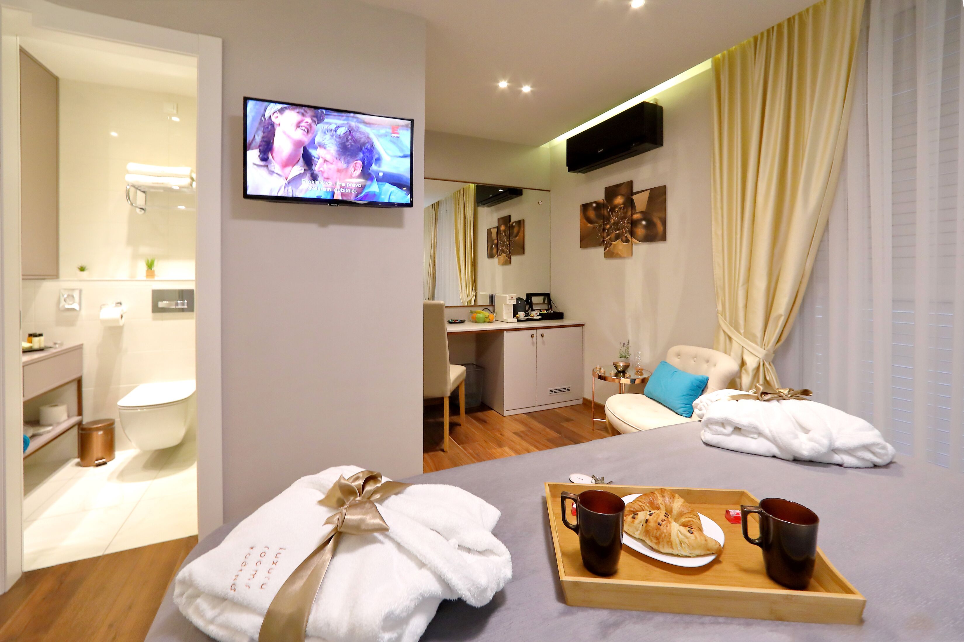 A hotel room with a bed, a TV, a breakfast tray, and a bathroom visible in the background.